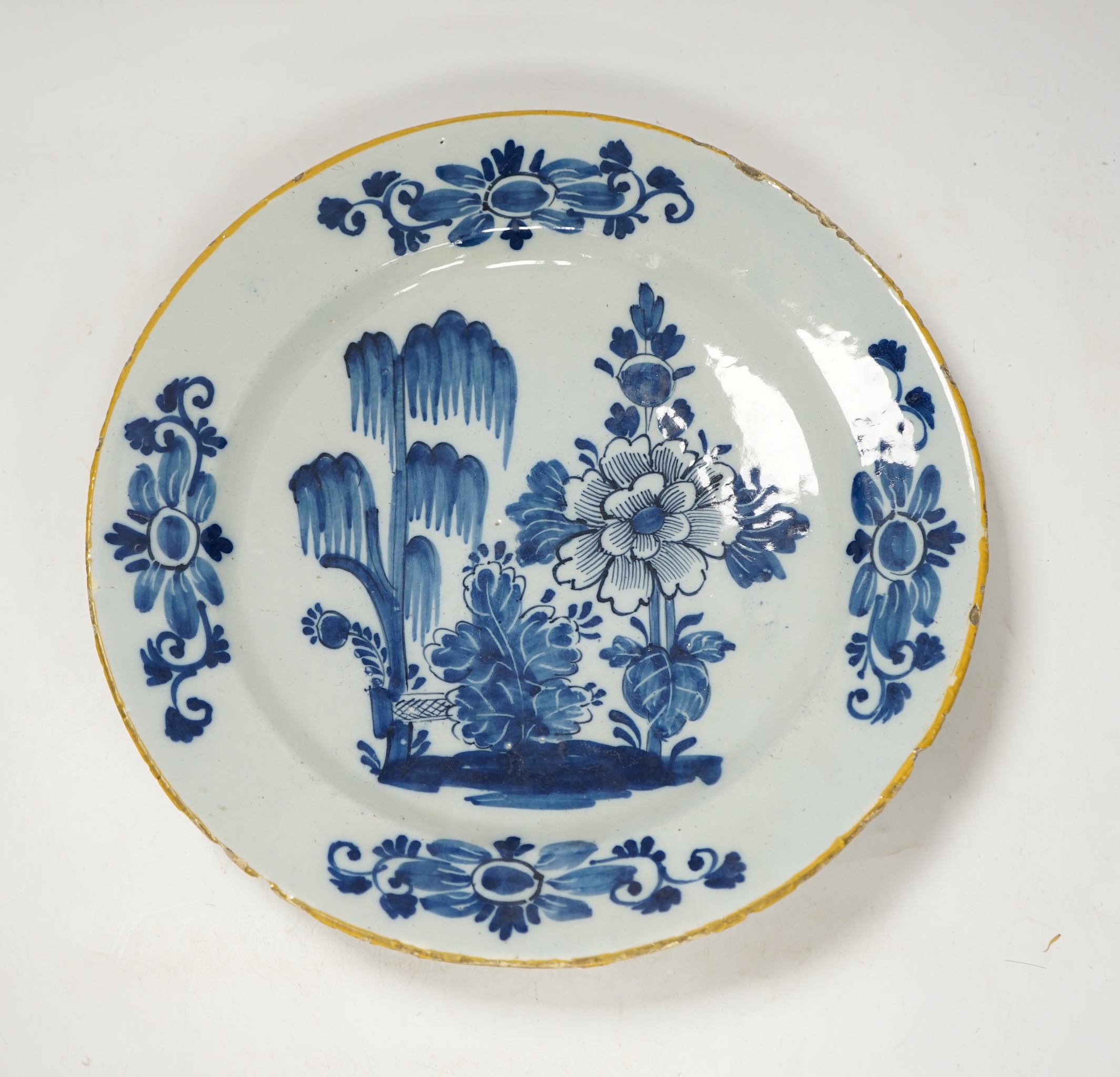 An 18th century delft blue and white dish, painted with a stylised peony and willow tree, 32cm diameter. Condition - fair, typical edge chipping all over